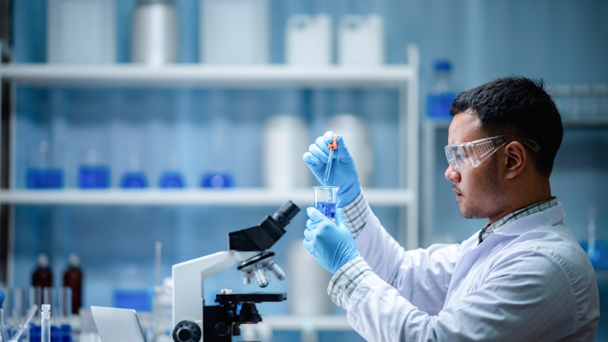 Pharmaceutical researcher conducting molecular biology experiment with microscope and beaker